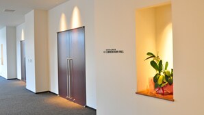 A hallway with doors leading to a convention hall, a potted plant, and a sign indicating the direction to the convention hall. - Rikuchu Kaigan Grand Hotel (Kamaishi)