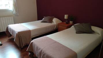 Two single beds with striped bedding, a nightstand with a lamp and a plant, and a window with curtains.