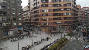 A multi-story residential building with balconies, a pedestrian walkway, and benches. - Pensión Arias (Bilbao)