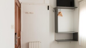 A room with a wooden door, a white radiator, a black TV mounted on the wall, and a white curtain. - Pensión Arias (Bilbao)