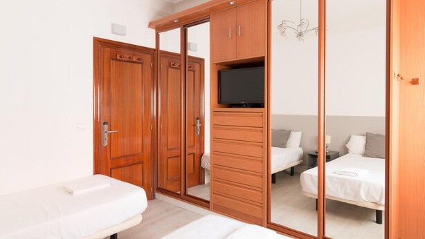 A bedroom with a large wardrobe, a television, and two beds. - Pensión Arias (Bilbao)