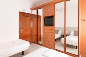 Une chambre avec une grande armoire, une télévision et deux lits.