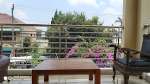A balcony with a metal railing, a wooden table, and a chair. - Villa Pribadi Beunying 35 pax (Cipanas)
