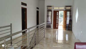 A hallway with a shiny tiled floor, a metal railing, and a red chair. - Villa Pribadi Beunying 35 pax (Cipanas)