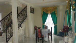 A dining area with a table and chairs, a staircase, and a window with green curtains. - Villa Abdi Cipanas with Swimming Pool (Cipanas)
