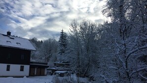 A traditional building with a snow-covered roof and a small stream flowing through a forested area. - Gasthof&Pension Brettmühle (Koenigswalde)