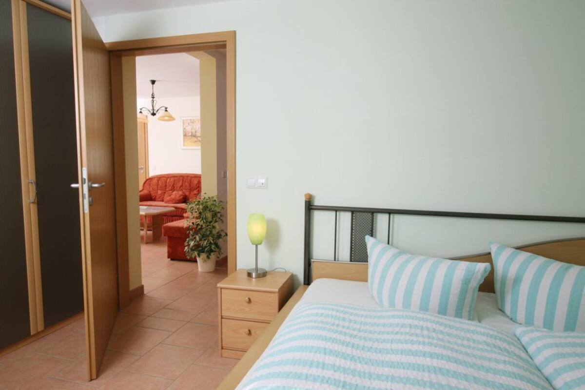 A bedroom with a bed, bedside table, and a nightstand. There is a door leading to another room.