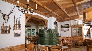 A rustic dining area with wooden furniture, a green tiled stove, and antler decorations. - Gasthof&Pension Brettmühle (Koenigswalde)