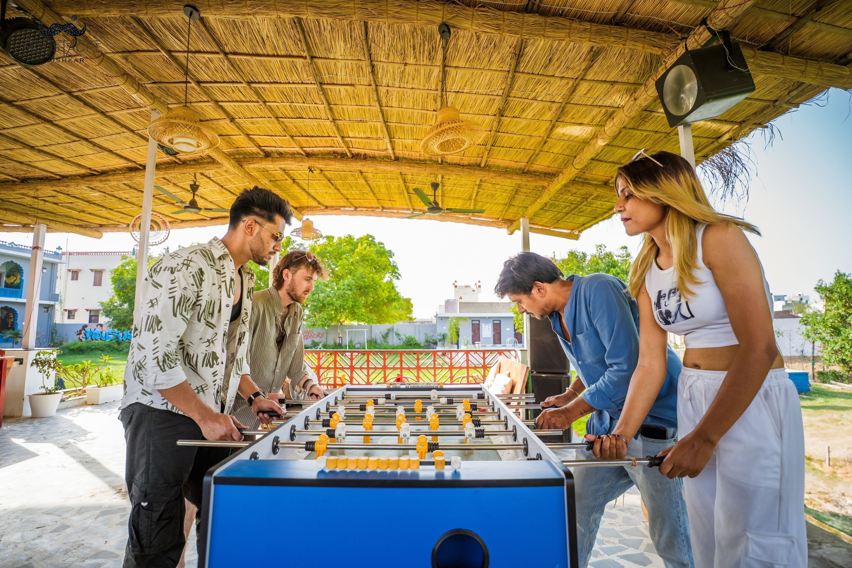 A group of people playing foosball under a thatched roof structure.