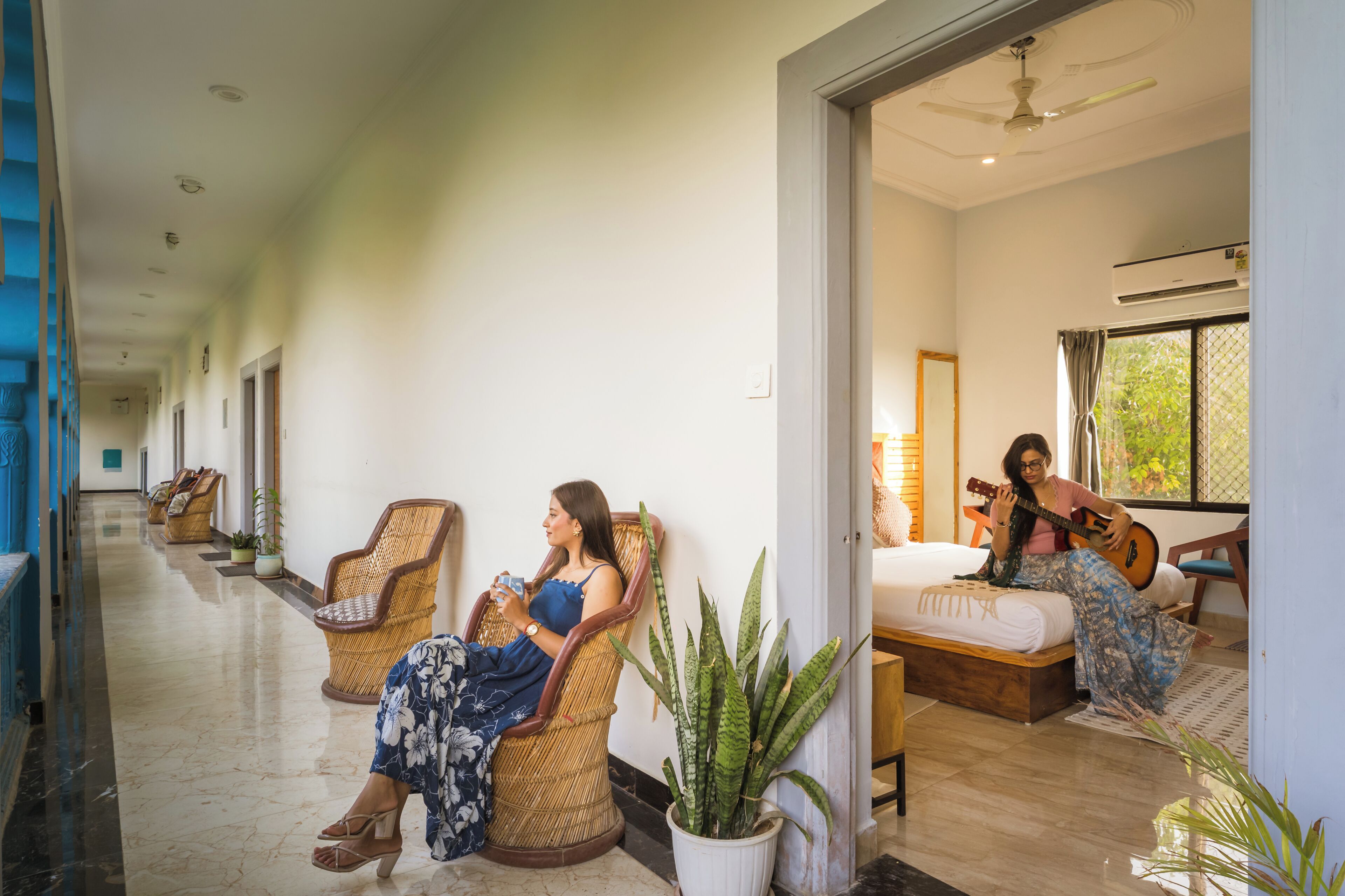 A corridor with wicker chairs, a bed with a guitar, and a potted plant.