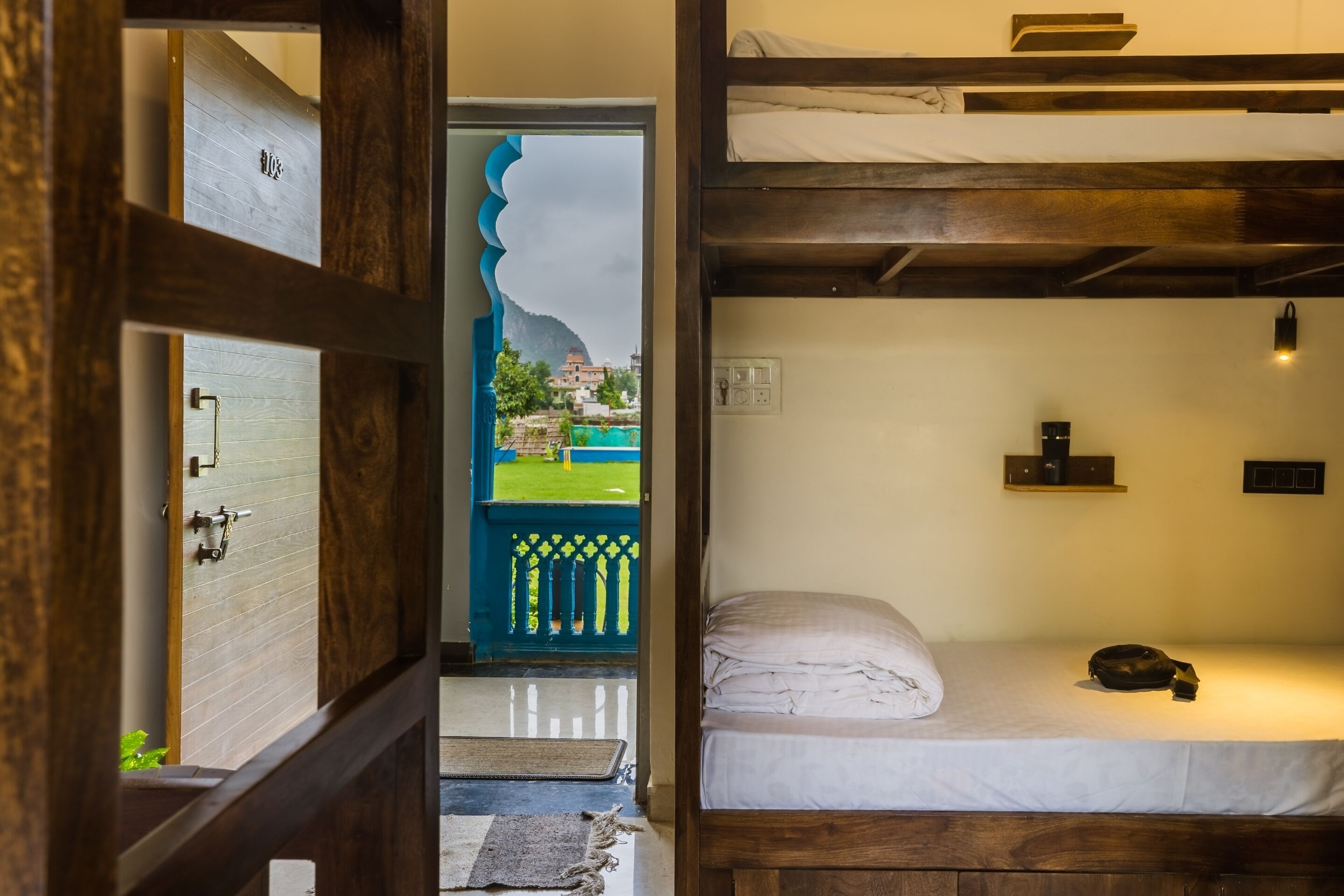 A room with a bunk bed, a door leading to a balcony, and a view of a green landscape.