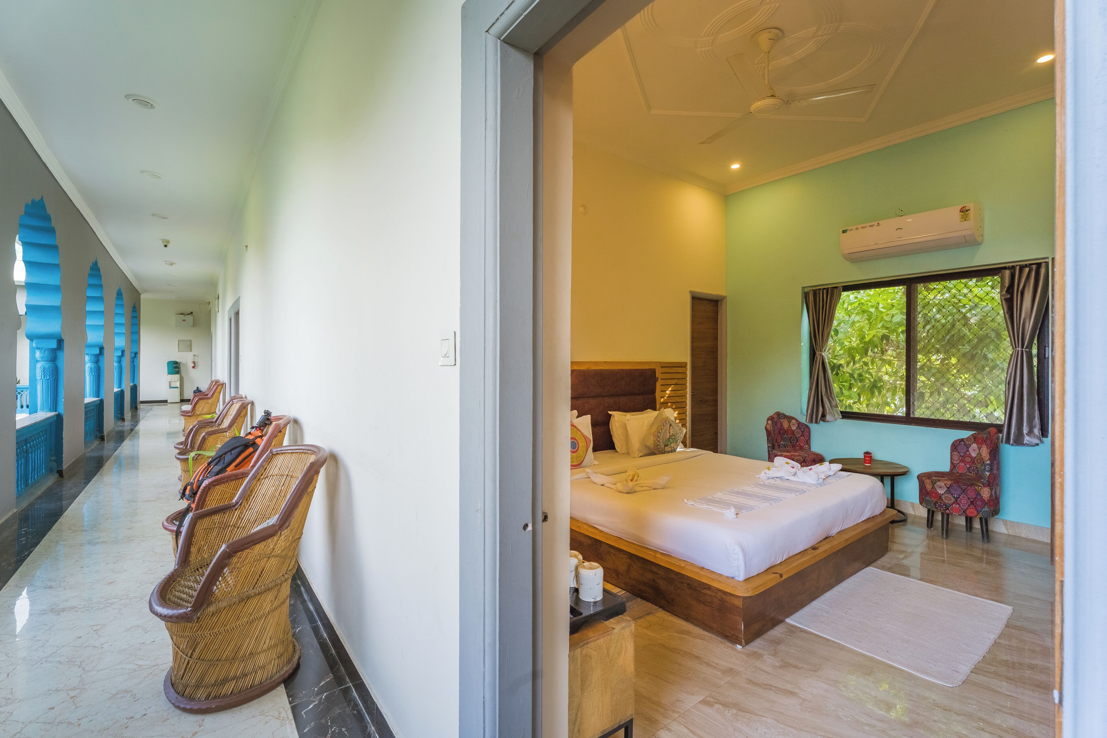 A hotel room with a bed, a window with curtains, a small table, and a chair.