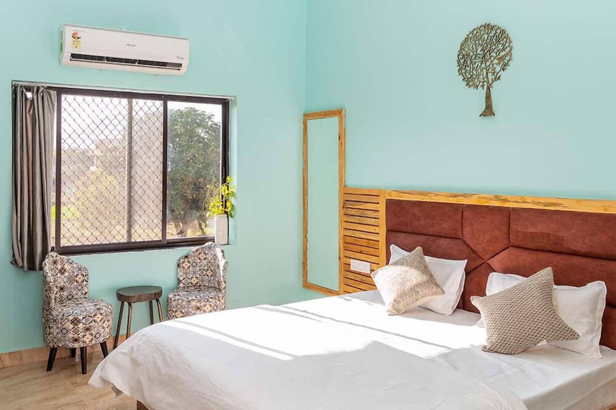A bedroom with a bed, two chairs, a window with curtains, an air conditioning unit, and a wall-mounted tree decoration.