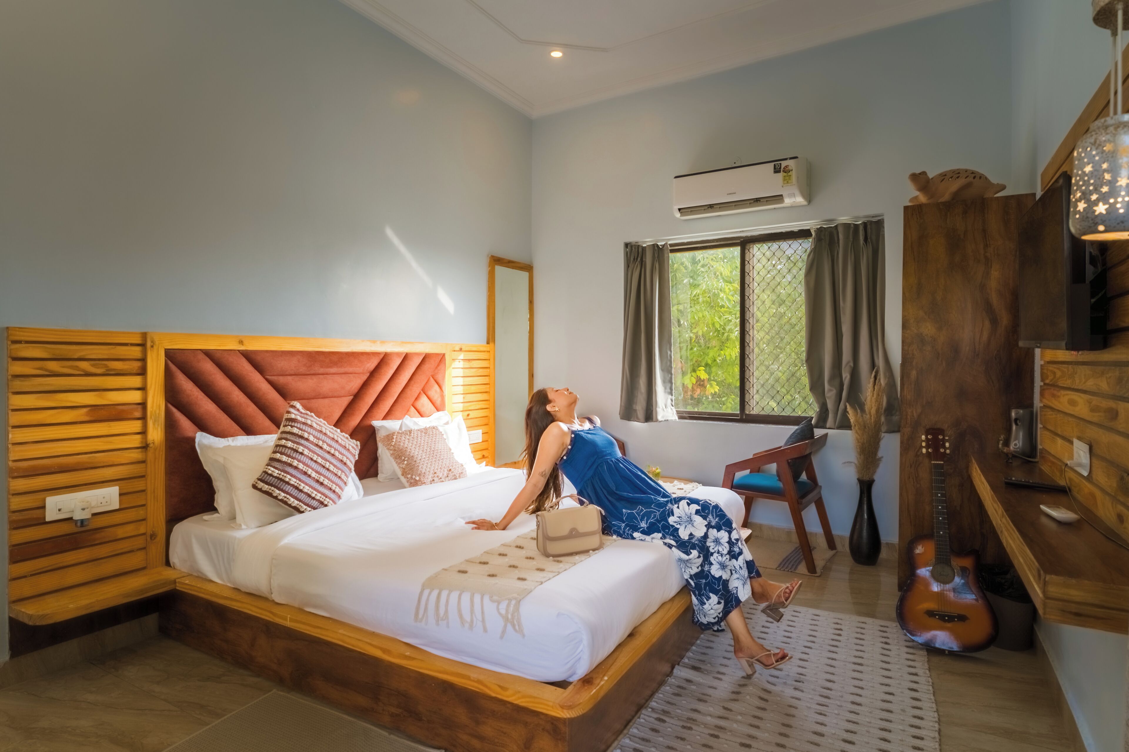 A bedroom with a large bed, a guitar, and a window with curtains.