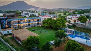 A courtyard with a volleyball court, a swimming pool, and a building with traditional architecture. - Moustache Pushkar - Hostel (Pushkar)