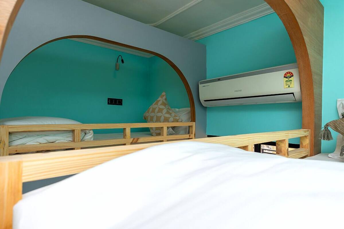A room with a wooden arched ceiling, a bed with a white mattress, a wooden bench, and an air conditioning unit on the wall.