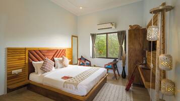 A bedroom with a large bed, a wooden headboard, a desk, a chair, a window with curtains, and a wall-mounted air conditioner.