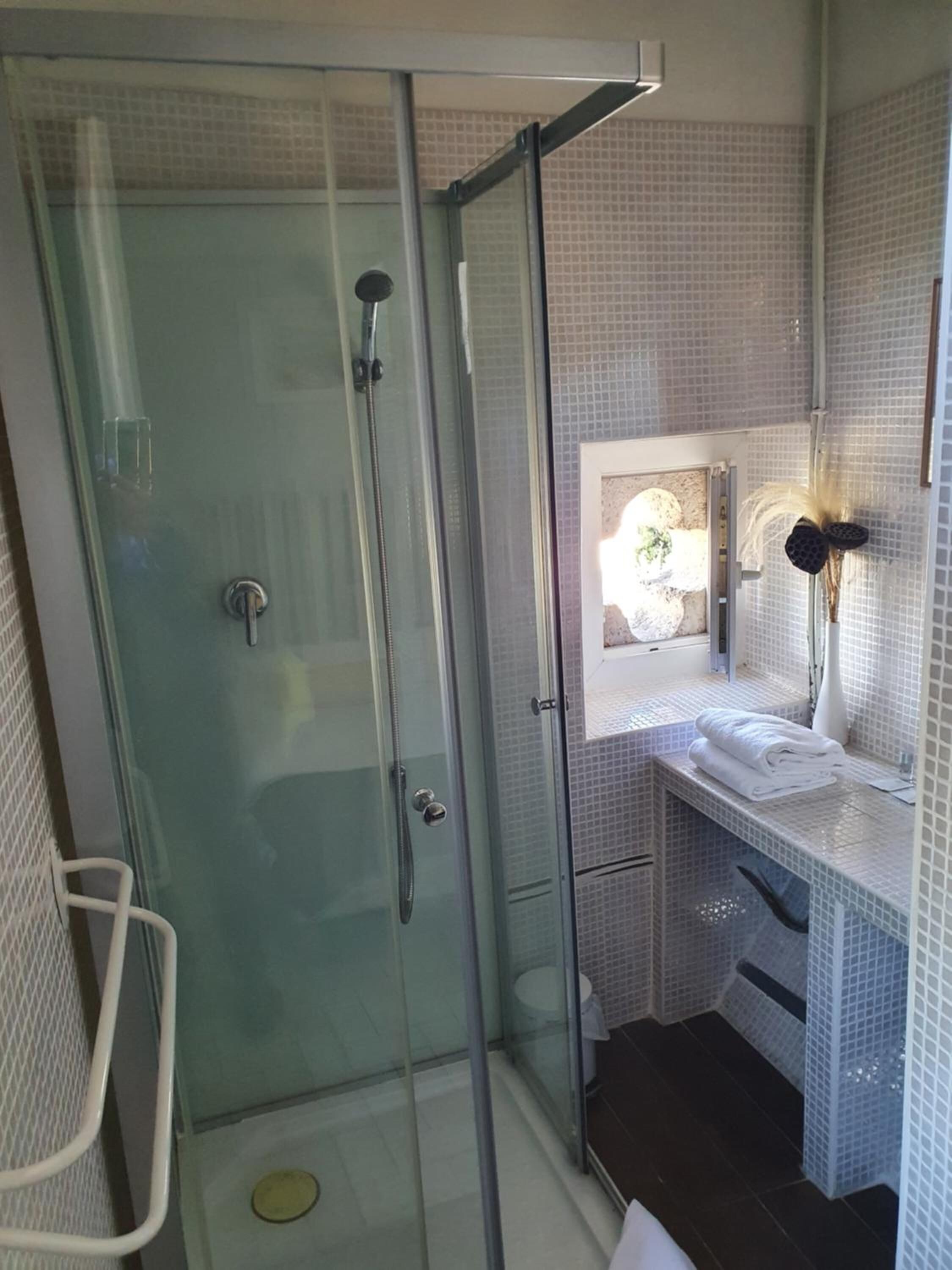 Un baño moderno con ducha de vidrio, un lavamanos blanco con espejo y una planta pequeña en el tocador.