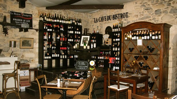 A wine cellar with wooden furniture and a stone wall. There are wine racks on the walls and a wooden cabinet with wine bottles. - Le Bistrot Vinaigrette (Prades-le-Lez)