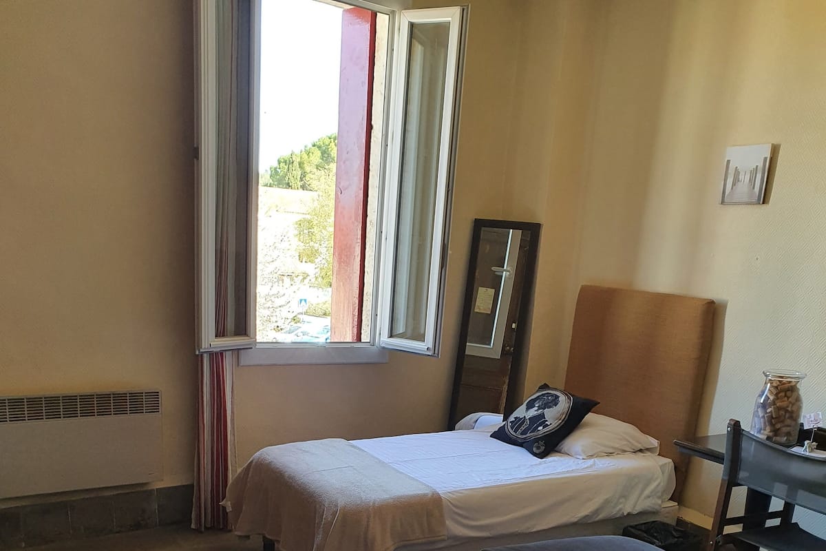 Quarto de hotel com duas camas, uma janela com cortinas, um aquecedor, uma mesa com um pote de lanches e um espelho na parede.