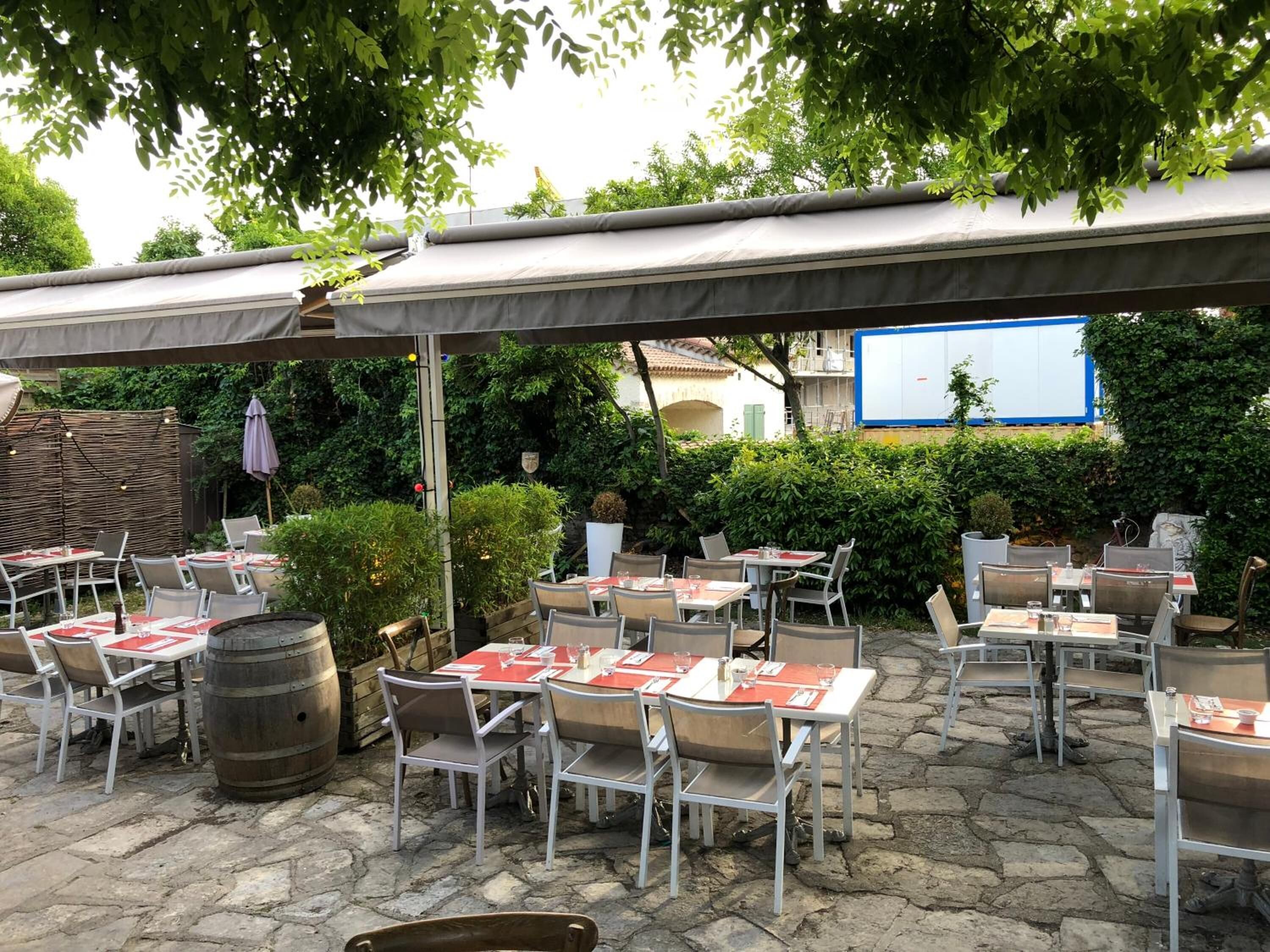 An outdoor patio with tables and chairs, a wooden barrel, and a whiteboard in the background.