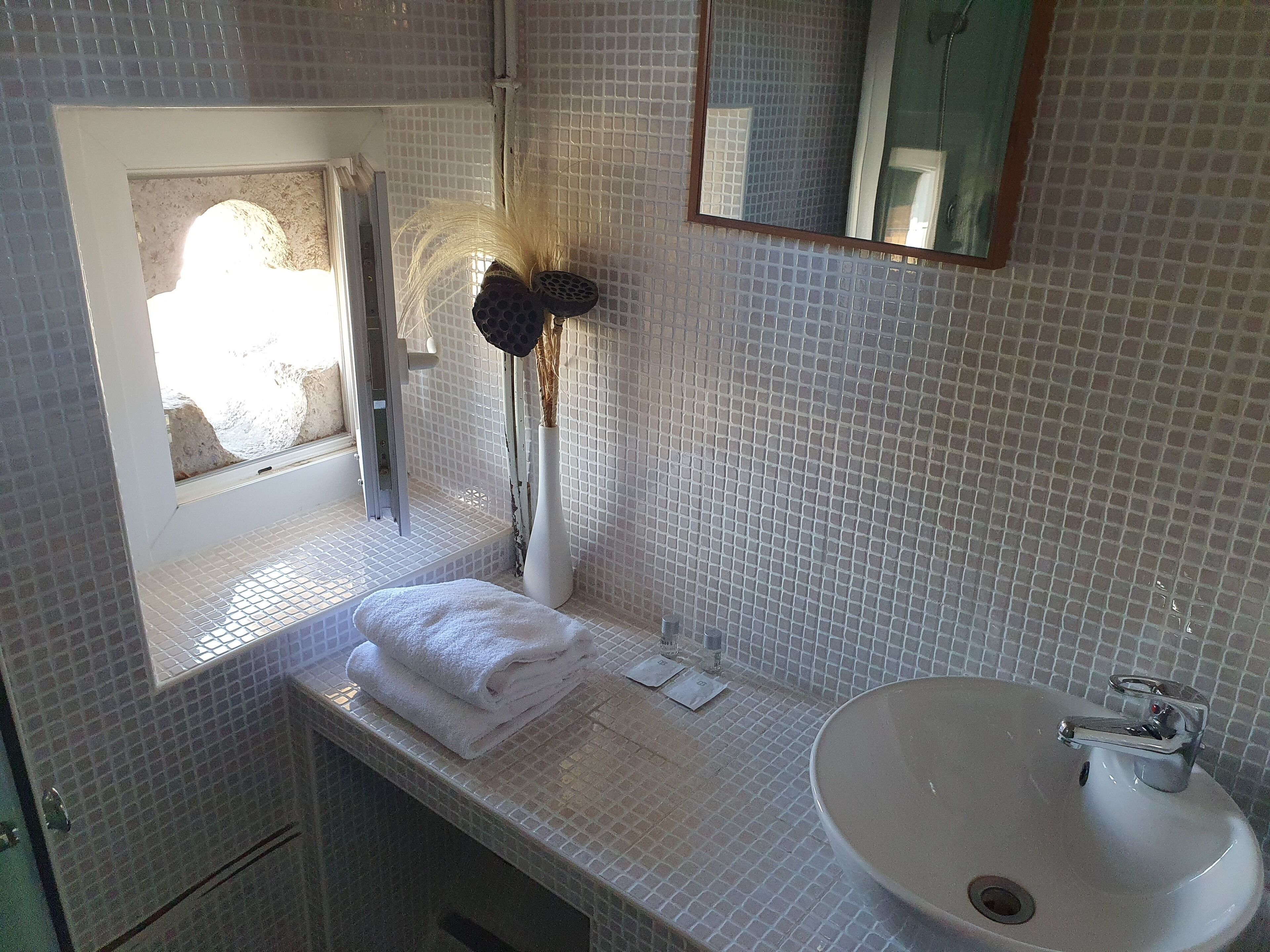 Een badkamer met een wit betegelde muur, een wastafel, een spiegel en een handdoek op het aanrecht.