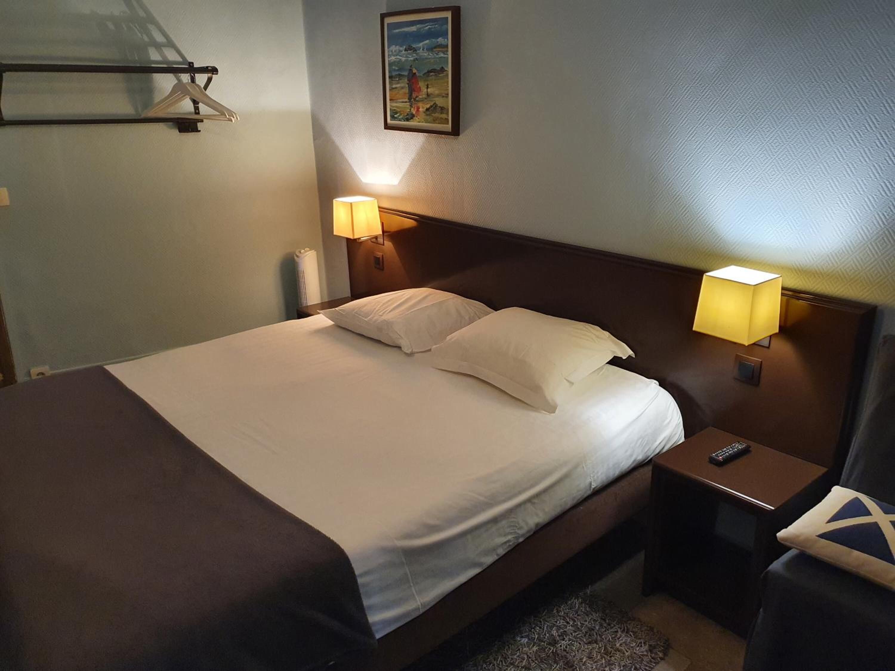 A neatly made bed with white linens and two pillows, flanked by bedside tables with lamps. A painting hangs on the wall above the bed.