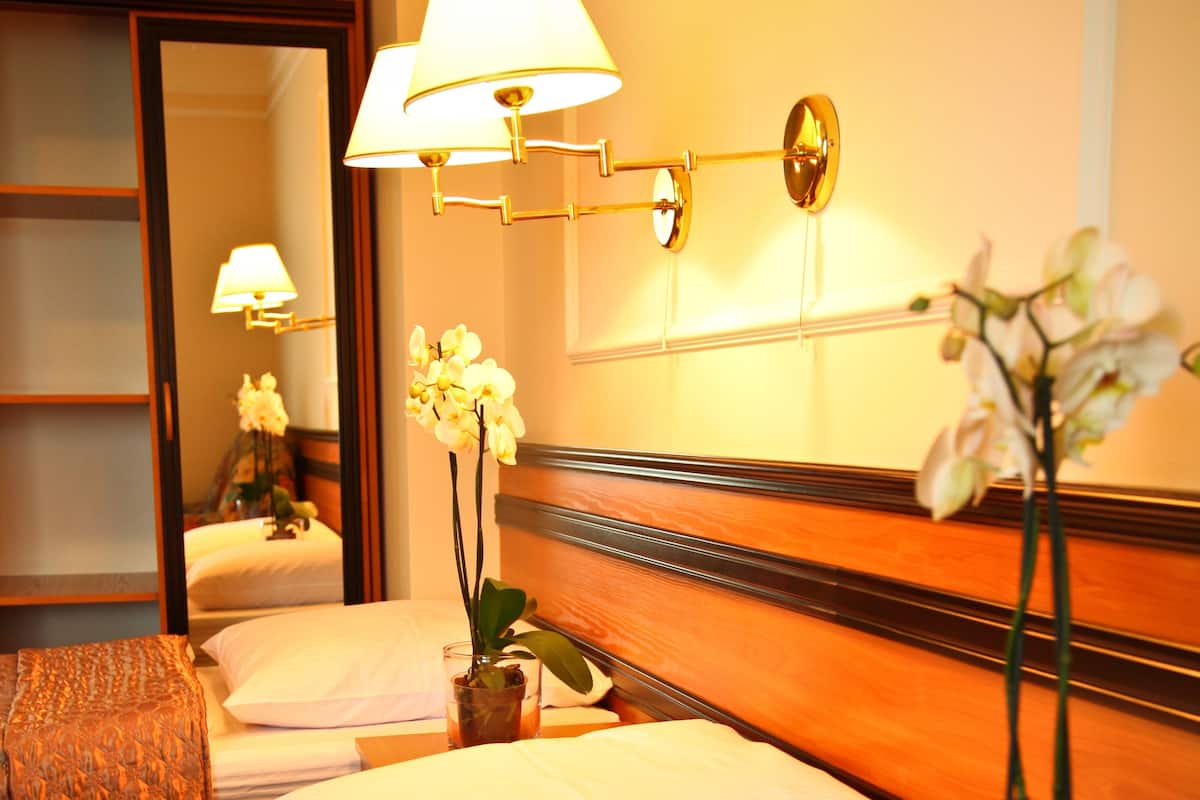 A hotel room with a wooden bed, white bedding, a nightstand with a lamp, and a potted orchid.