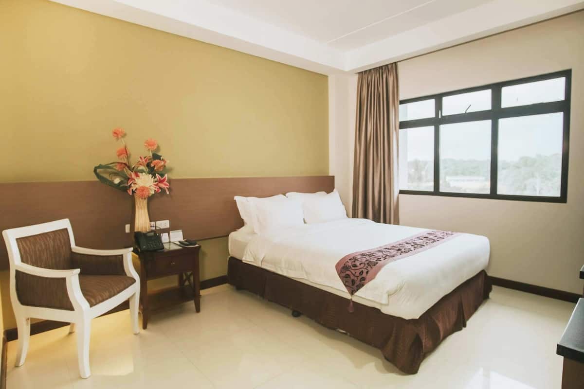 A hotel room with a bed, a desk with a telephone, a chair, and a window with curtains.