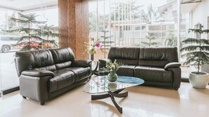 A modern living room with two leather sofas, a glass coffee table, and a large window offering a view of a residential area with palm trees and buildings. - Panorama Summit Hotel (Davao)