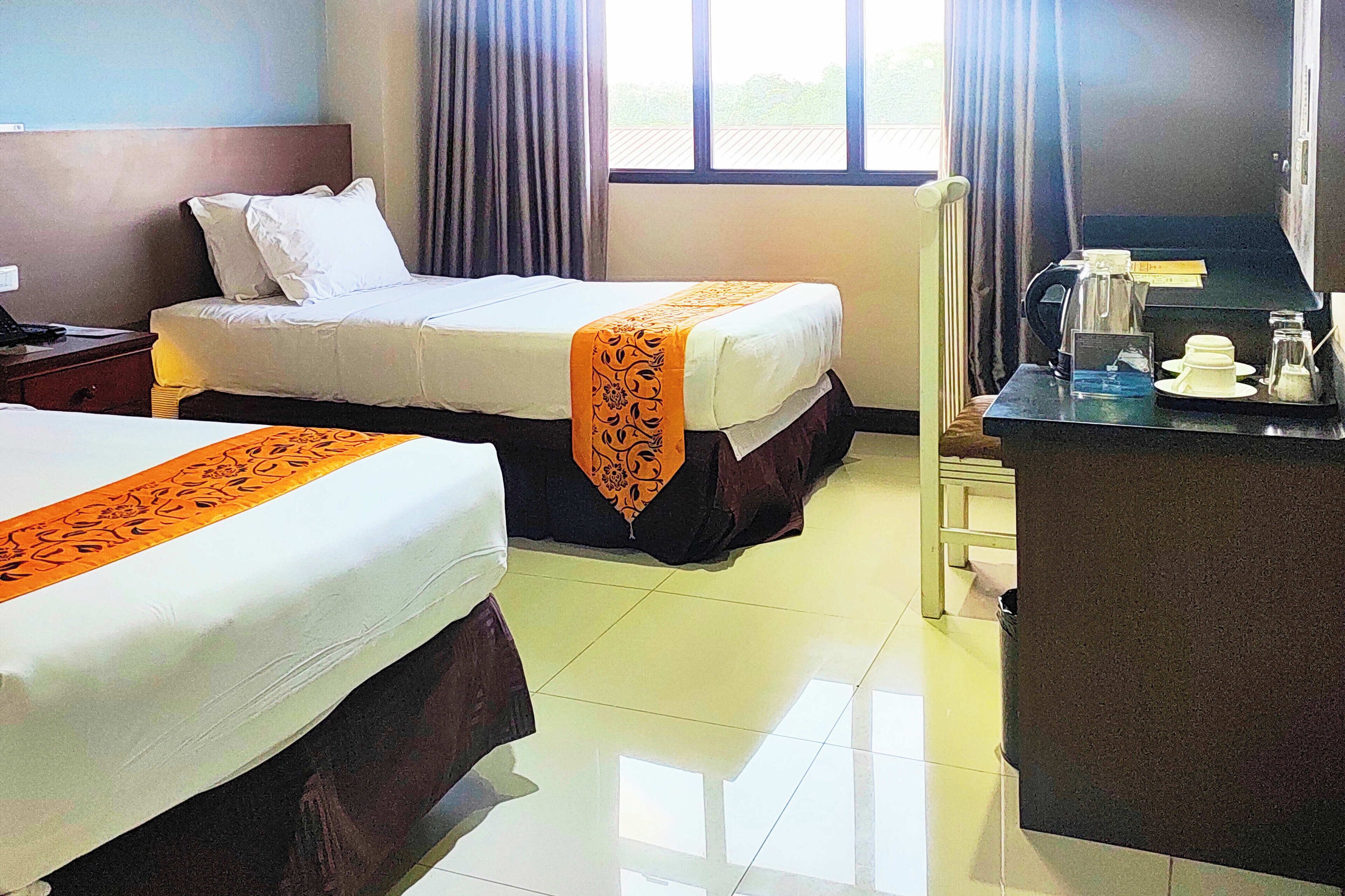 A hotel room with two beds, a desk with a coffee maker, and a window with curtains.