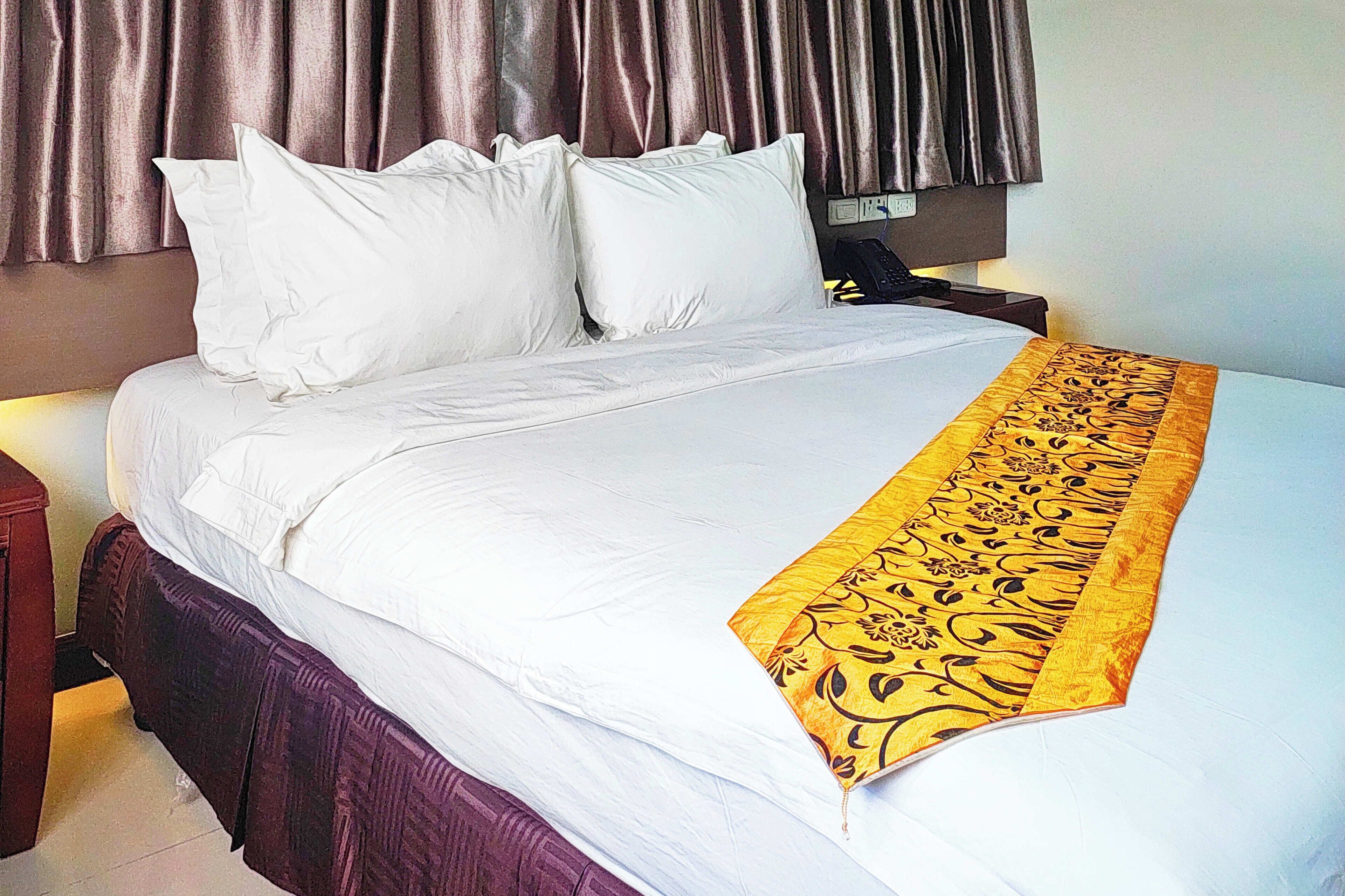 A neatly made bed with white linens and a decorative yellow and black runner.