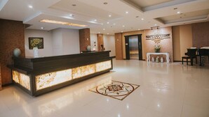 A hotel reception area with a modern reception desk, a wall-mounted sign, a piano, and a decorative floor pattern. - Panorama Summit Hotel (Davao)