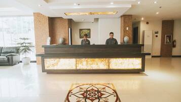 A hotel reception area with a modern design, featuring a reception desk, a large window, and a decorative floor pattern.