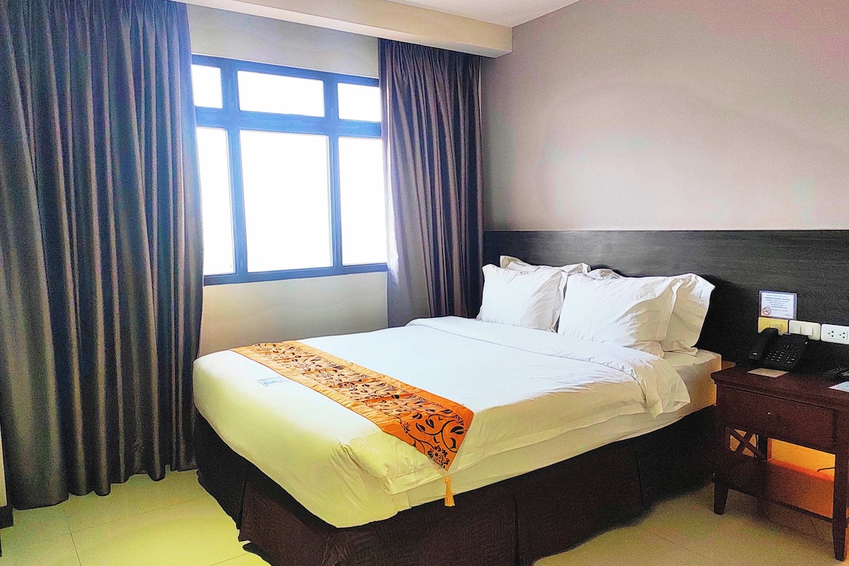 A hotel room with a bed, curtains, a nightstand, and a window.