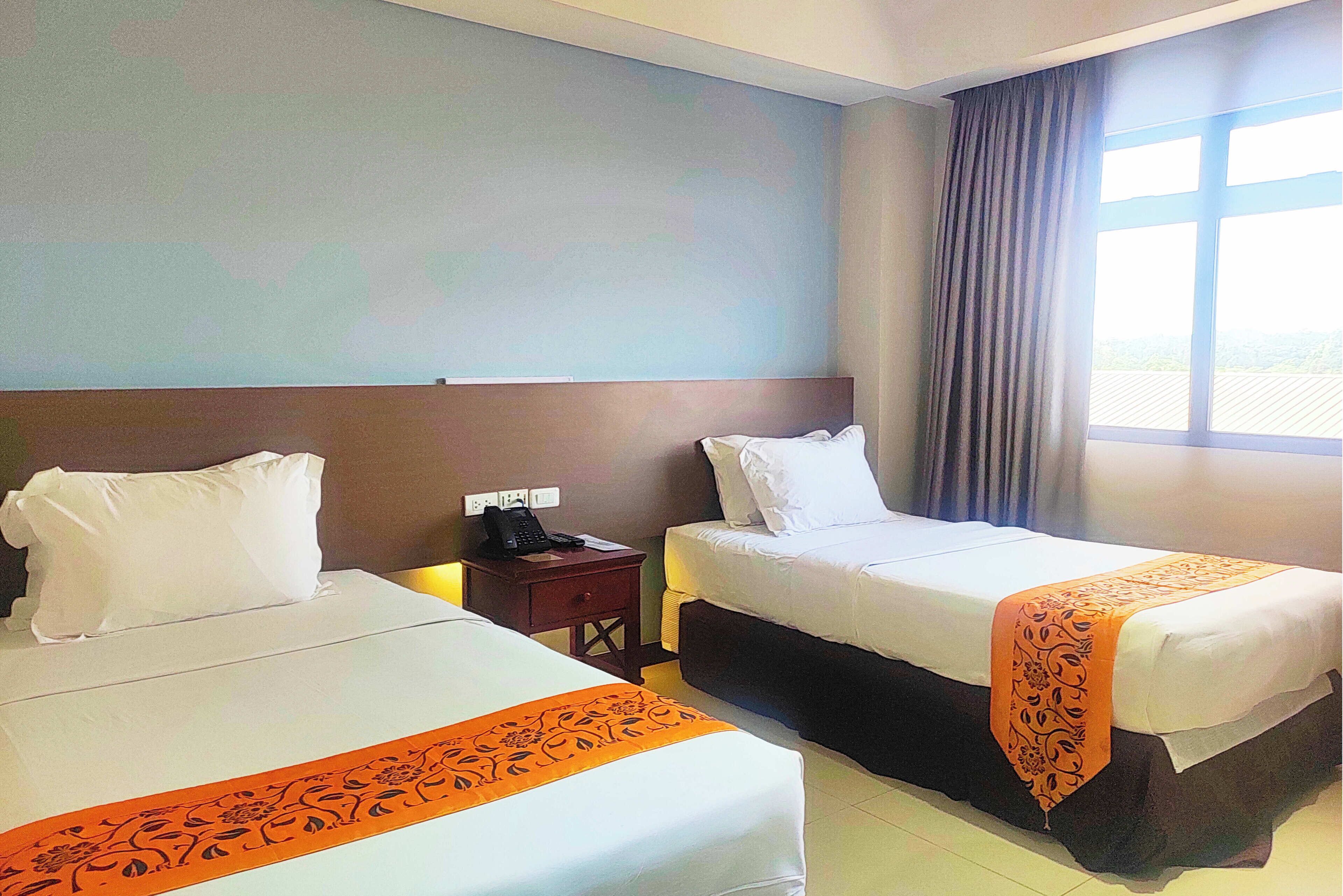 A hotel room with two beds, a nightstand, and a window with curtains.