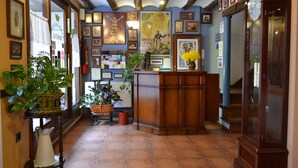 A lobby with a wooden reception desk, potted plants, framed pictures on the walls, and a large clock. - Hostal Santa Agueda (Tarazona)