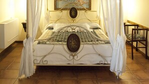 A four-poster canopy bed with a decorative headboard, a painting of cherubs above it, and a small table beside the bed. - Hostal Santa Agueda (Tarazona)