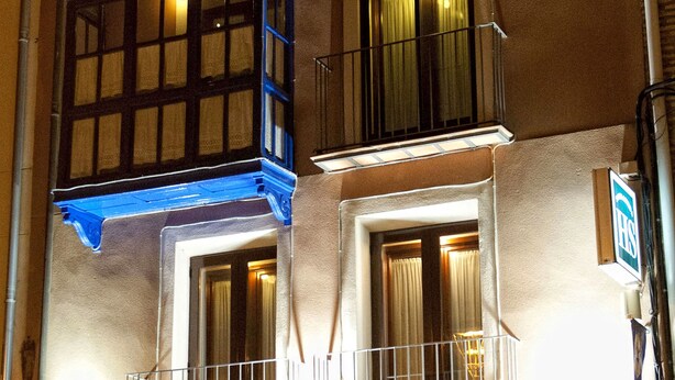 A two-story building with a ground-floor entrance labeled "HOTEL SANTA AGUEDA." There is a balcony with railings on the second floor, and a bench is visible outside the entrance. - Hostal Santa Agueda (Tarazona)