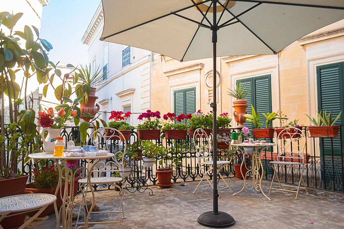 An outdoor café with tables and chairs, surrounded by potted plants and flowers.