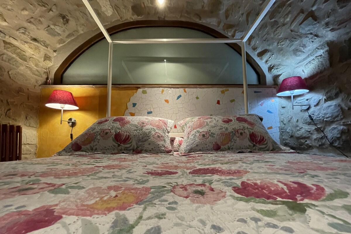 Ein Schlafzimmer mit Steinwand, gewölbter Decke, einem Bett mit Blumenmuster-Bettwäsche und zwei Wandleuchten.