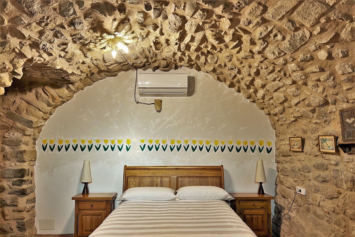 Ein Schlafzimmer mit Steinwand, einem Bett mit Holz Kopfteil, zwei Nachttischen mit Lampen und einem Wandbehang.