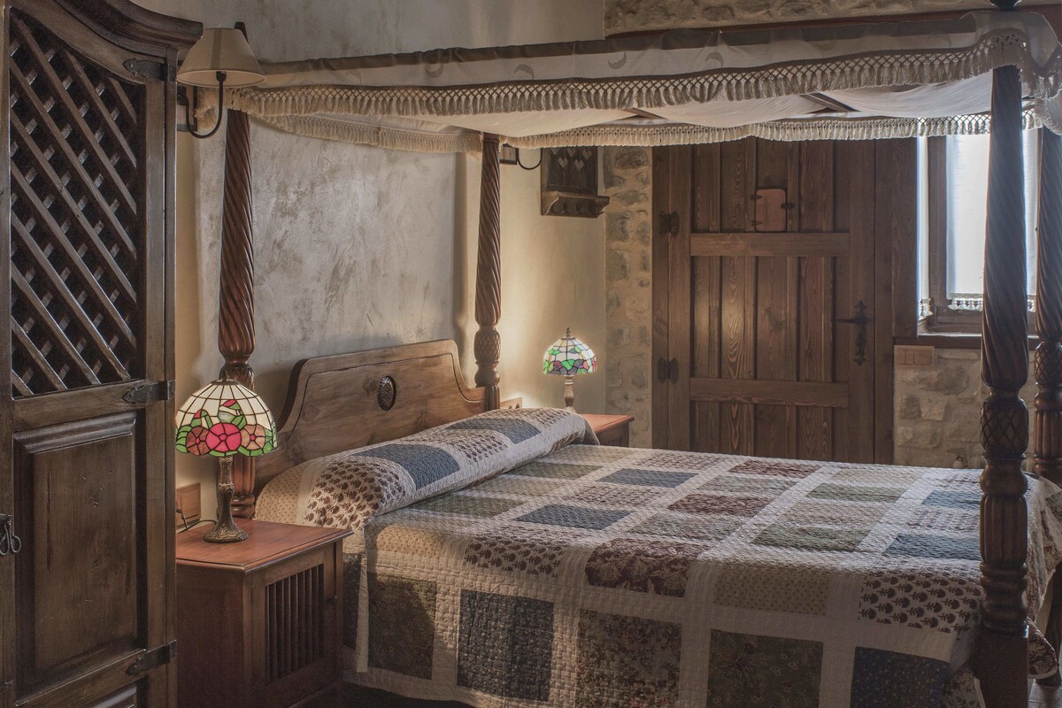 Ein traditionell eingerichtetes Schlafzimmer mit Himmelbett, Holzschrank und einer Tiffany-Lampe.