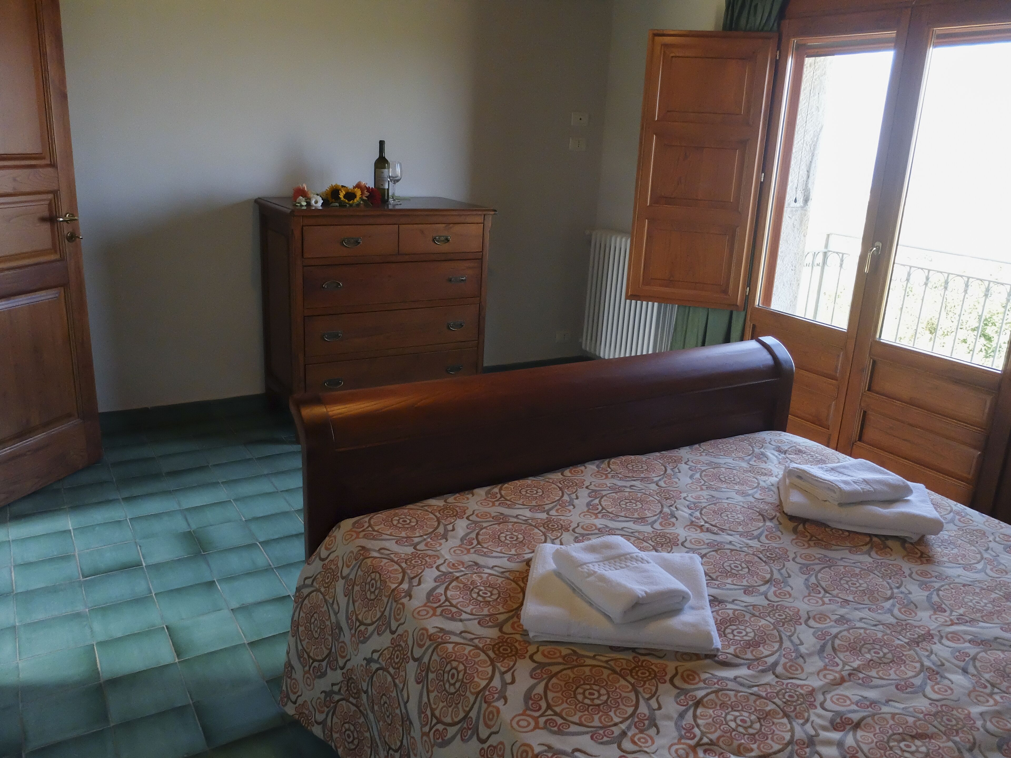 Une chambre à coucher avec un lit, une commode en bois, un radiateur et une fenêtre donnant sur un beau paysage.