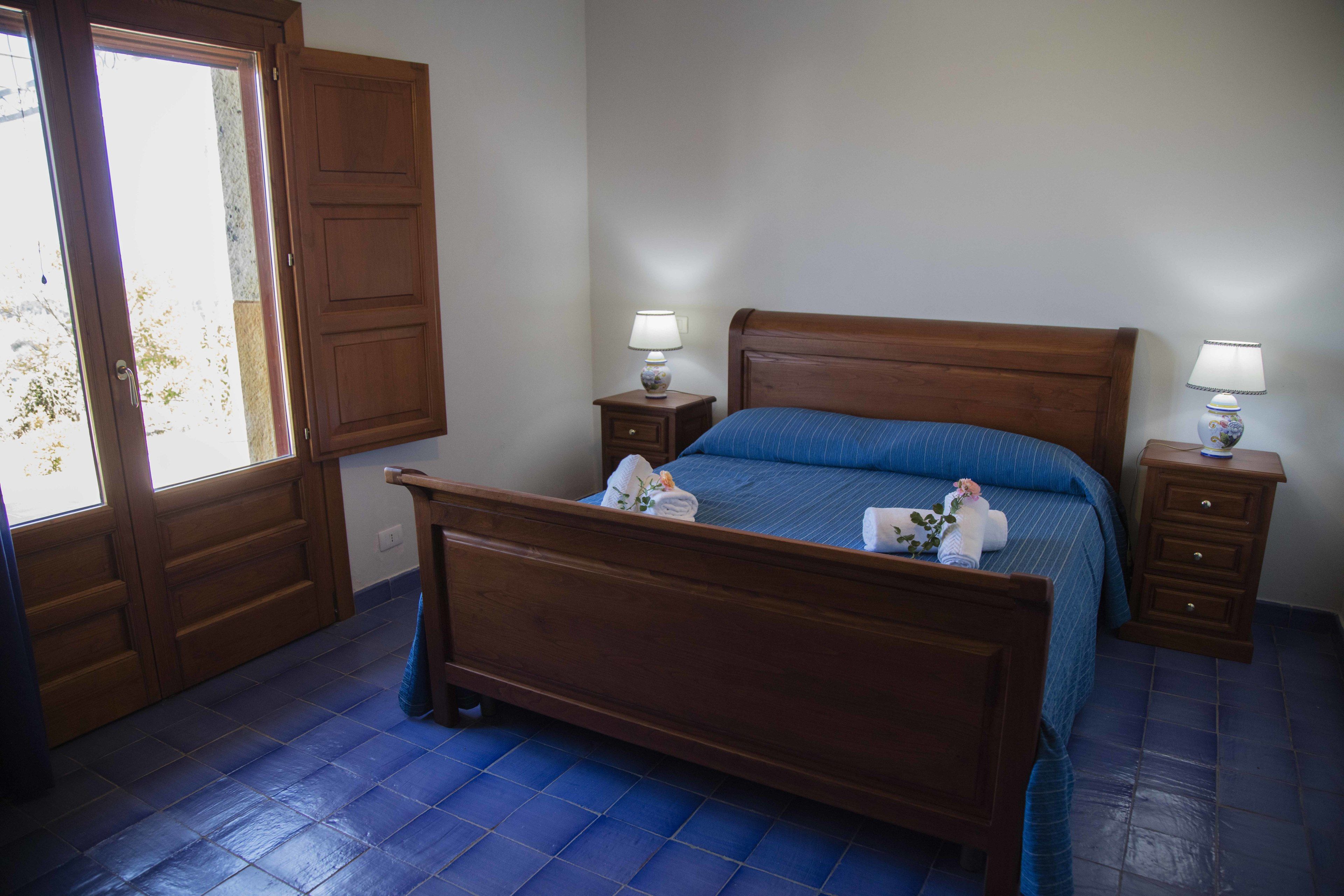 A bedroom with a wooden bed, two bedside tables with lamps, a window, and a door.