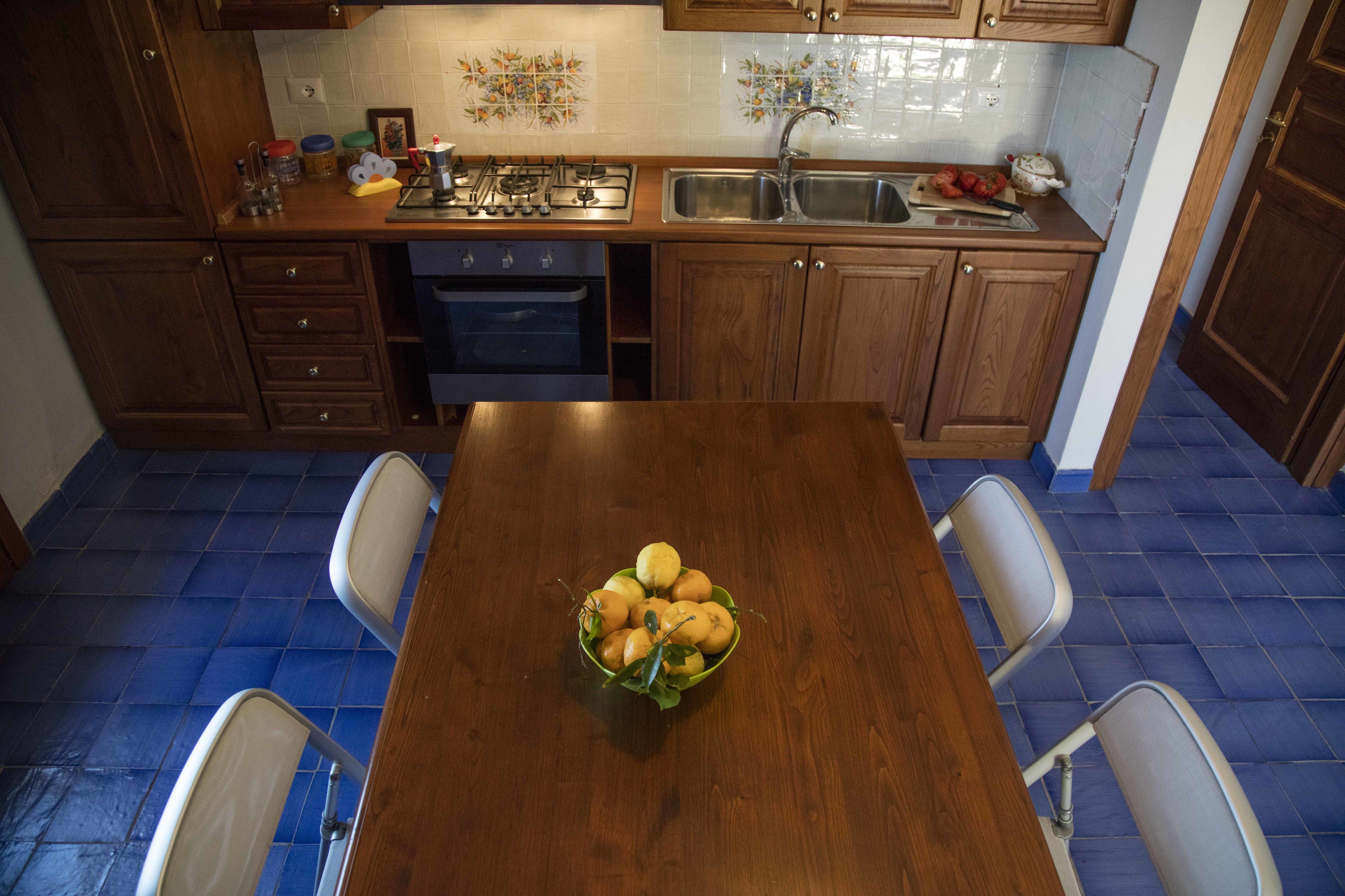 A kitchen with wooden cabinets, a stove, and a sink. There is a table with a bowl of fruit in the center.