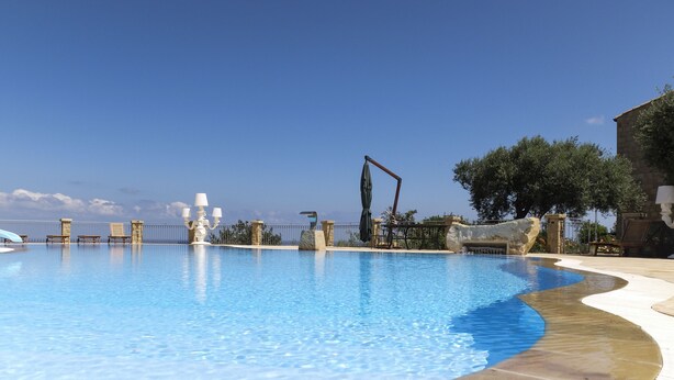 A large swimming pool with a curved edge, surrounded by lounge chairs and a stone wall. - Terrazze sul Tirreno (Lascari)