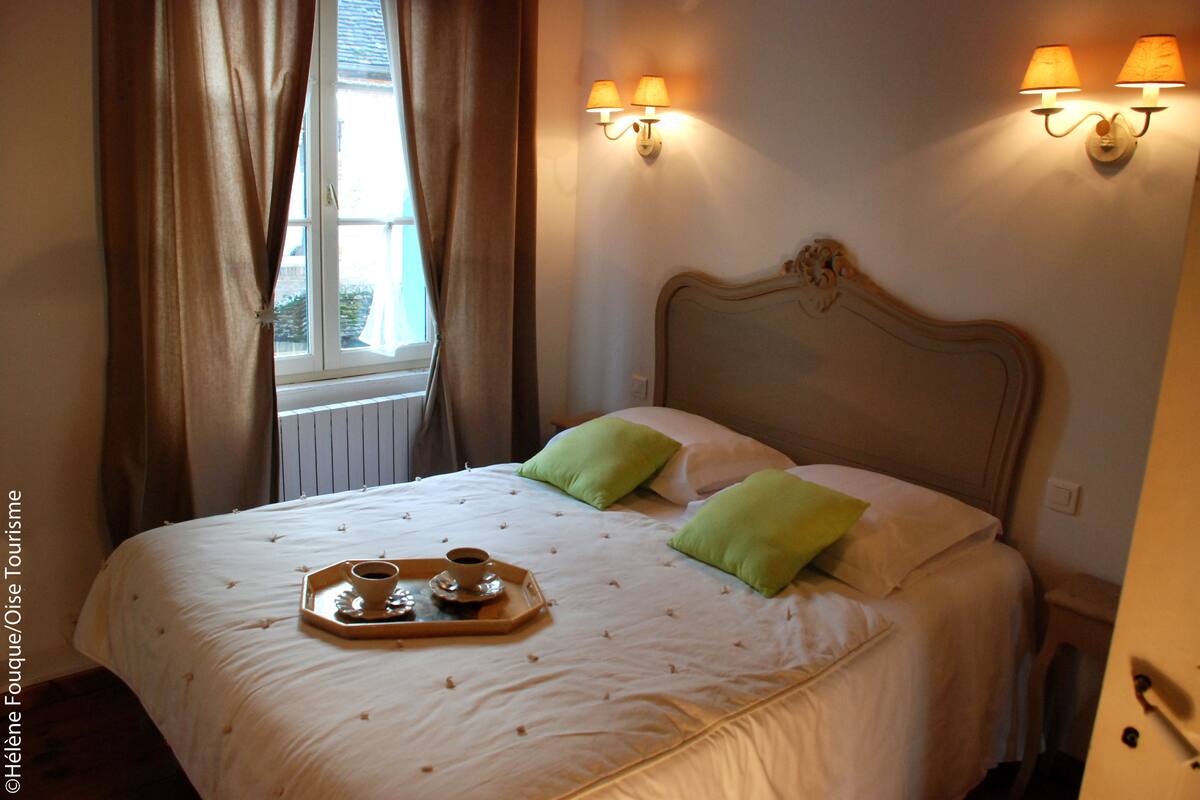 A hotel room with a bed, two green pillows, a tray with a cup and saucer, and wall-mounted lamps.