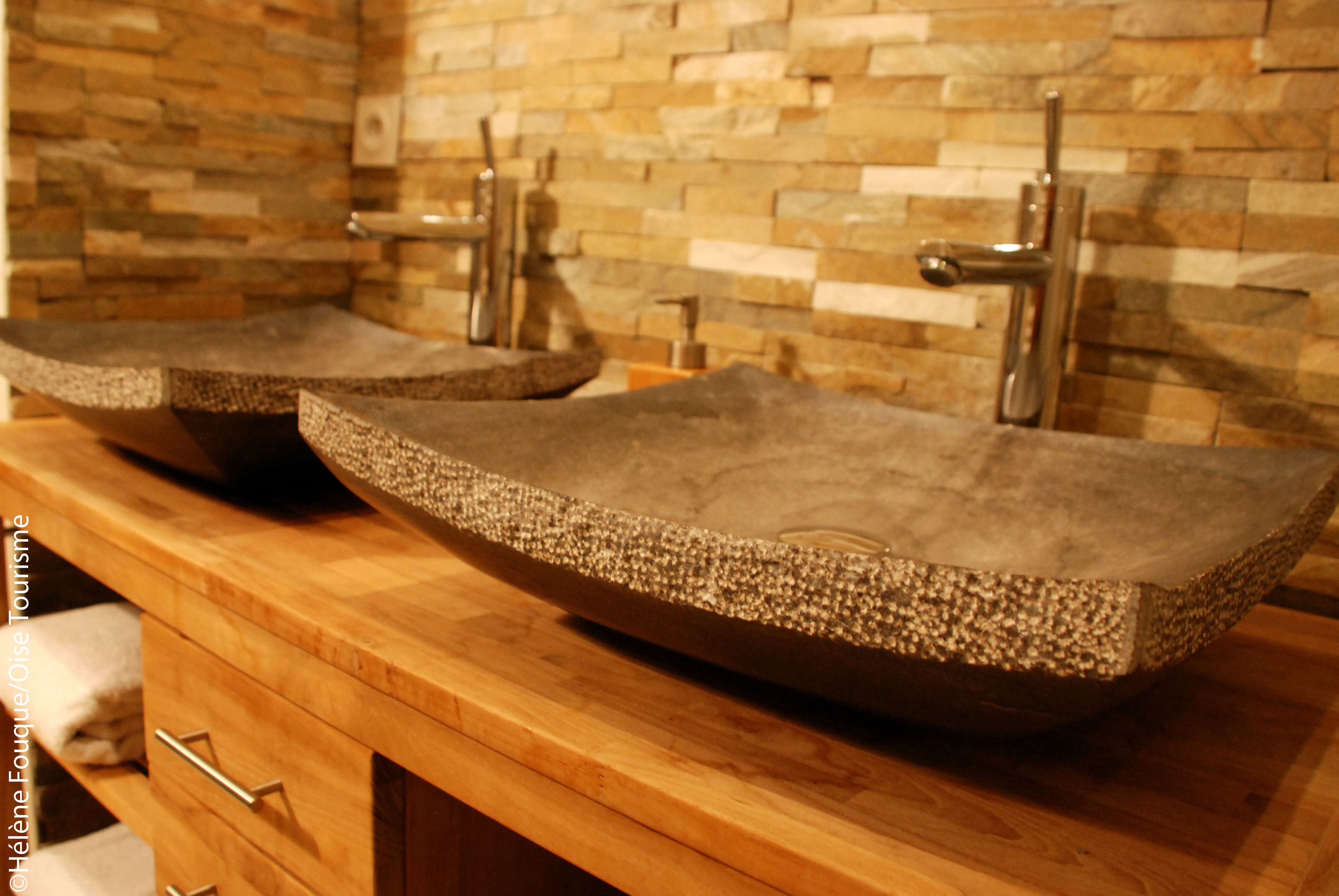 Un baño con dos lavamanos grandes de piedra texturizada sobre una encimera de madera.
