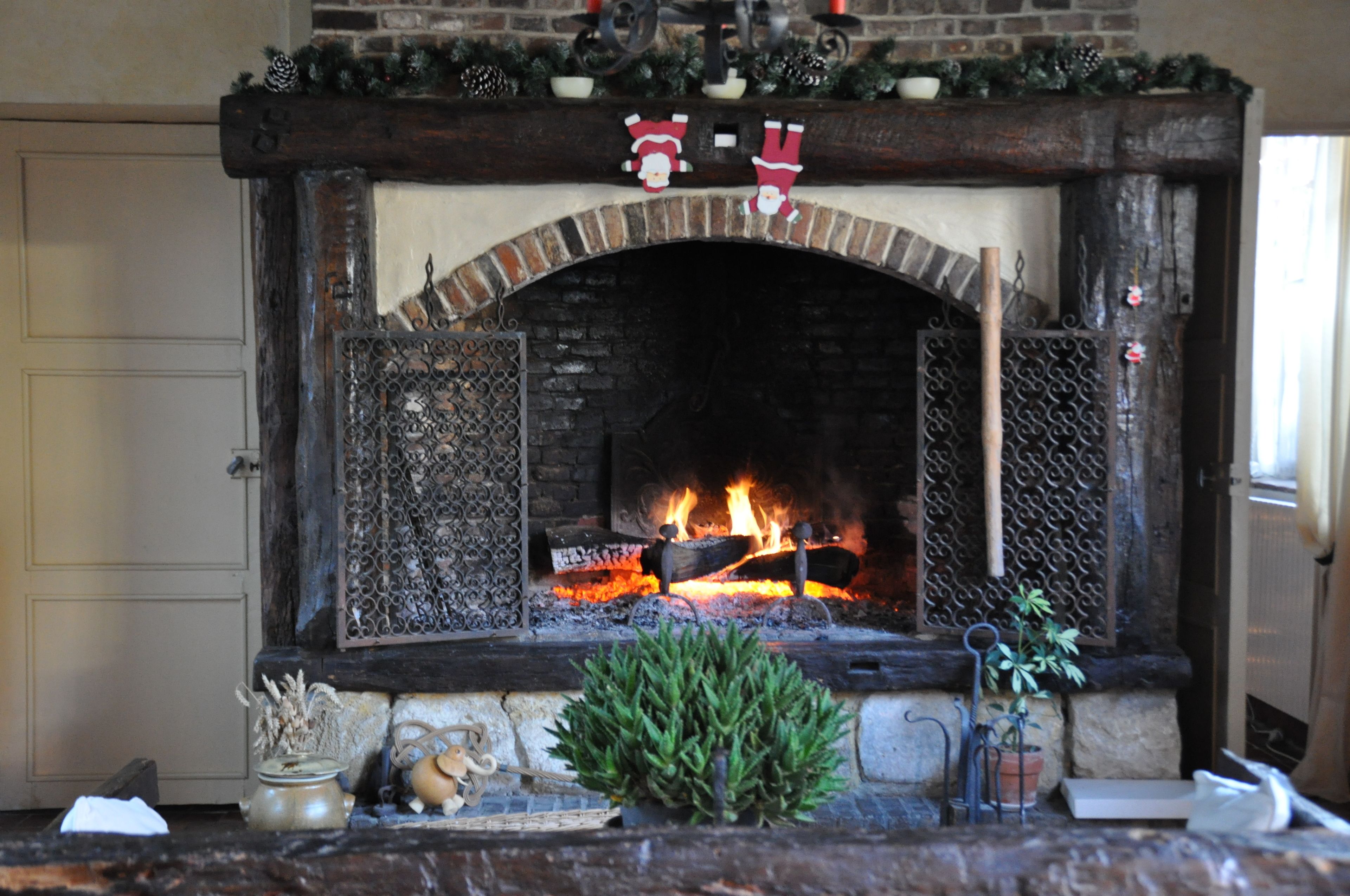 Une cheminée avec un foyer en briques, une étagère décorée d’ornements de Noël et un feu qui crépite à l’intérieur.